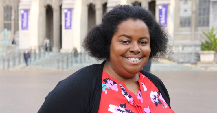 Amanda Bradley wears a bright red shirt and smiles in front of Suzzallo Library