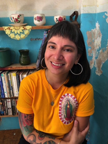 Diane Lopez sitting in a room with bookshelves wears a bright yellow shirt and smiles at the camera.